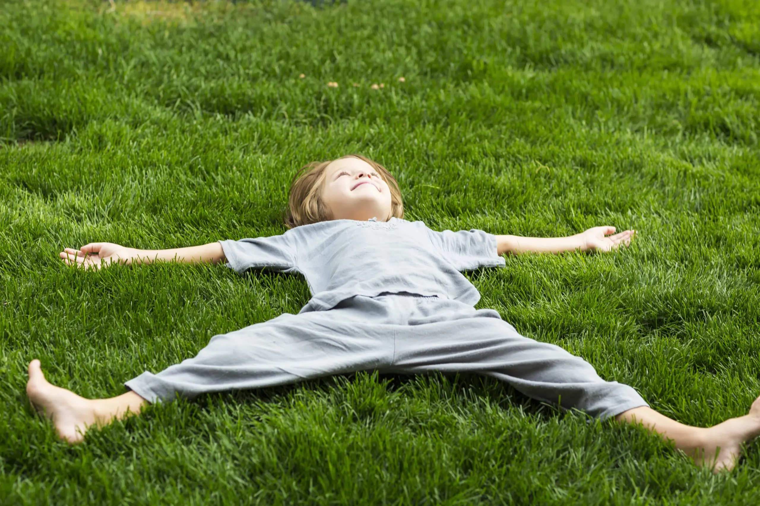 A young child lying back on a thick, healthy green lawn with arms outstretched